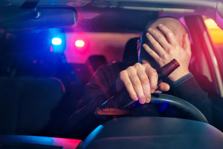 a drunk driver clutching a bottle  while driving