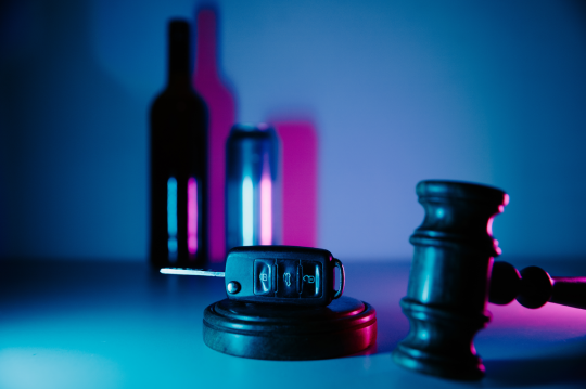Car key, gavel and alcohol drinks in neon light. Dangerous driving and law