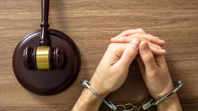 Handcuffed Convict, Law offender and Justice. Court sentence Prison. Handcuff locked and judge gavel on a wooden table, top view.
