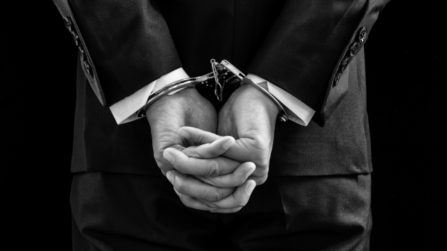 Arrested business man handcuffed hands at the back. Black and white