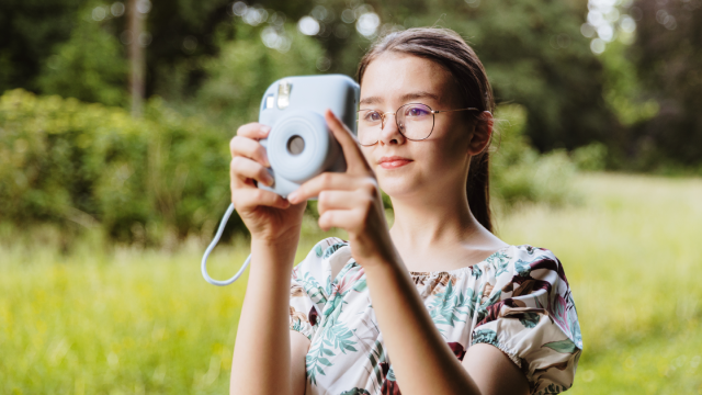 A beautiful girl takes pictures with a camera in the park.