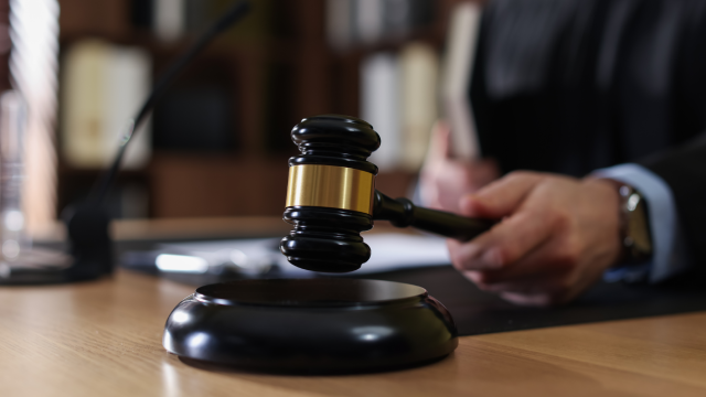 Judge striking gavel at wooden table indoors, selective focus