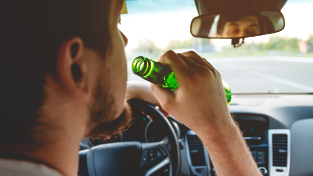 Drunk young man driving a car with a bottle of beer. Don't drink and drive concept. Driving under the influence. DUI, Driving while intoxicated. DWI